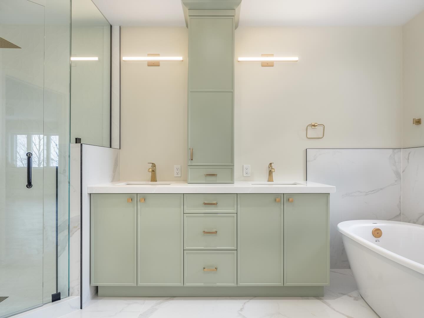 A modern bathroom designed by a top contractor features a mint green double-sink vanity, gold fixtures, a frameless glass shower on the left, a white freestanding bathtub on the right, and gold hardware accents throughout.