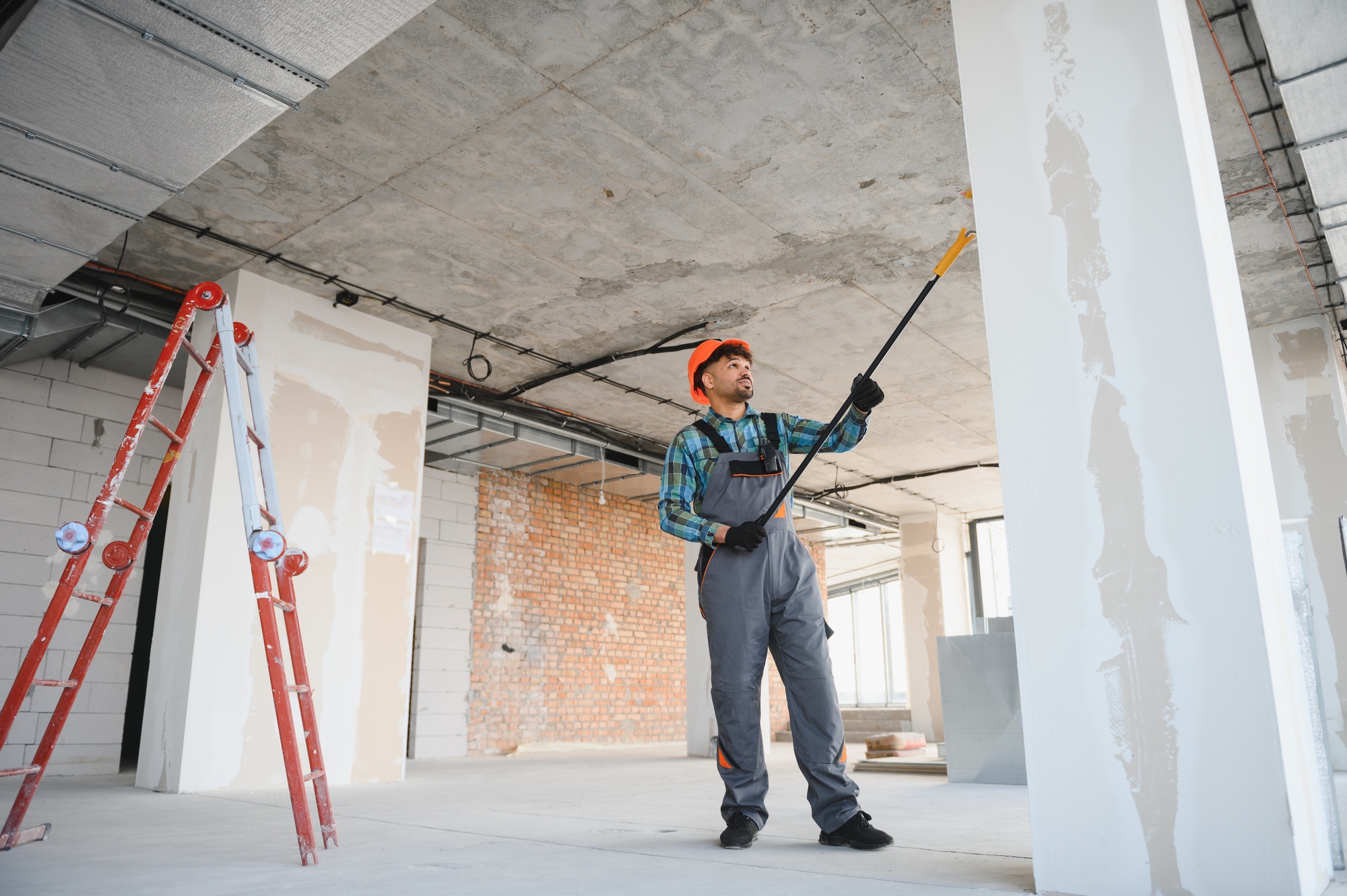 Construction worker painting walls and ceiling with telescopic paint roller