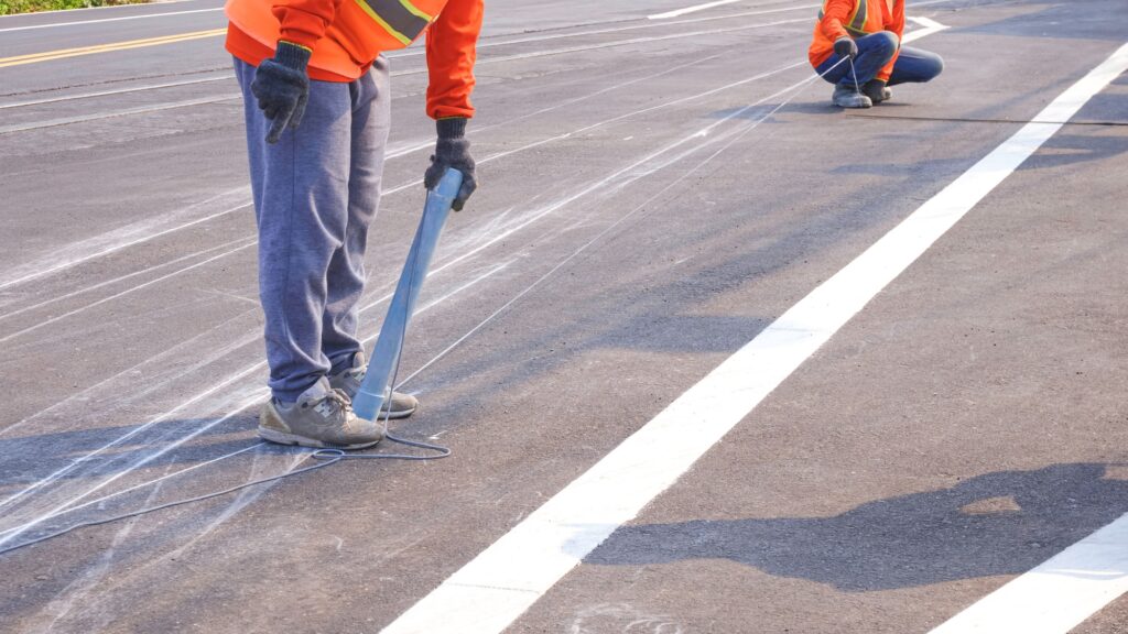 Cropped image of 2 road workers marking line for painting traffic color lines on asphalt road