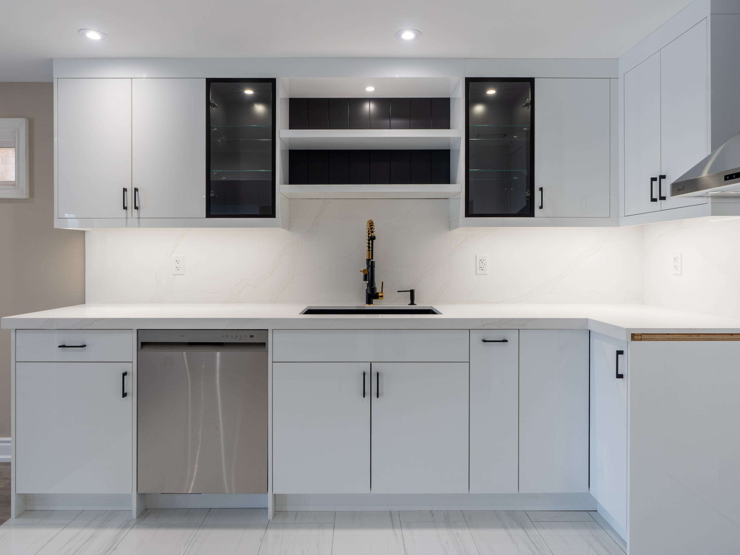 Modern kitchen features white cabinets, black handles, a stainless steel dishwasher, marble-look countertops and backsplash, plus a black faucet under open shelving with glass-front uppers—perfect inspiration for home renovations in Vaughan.